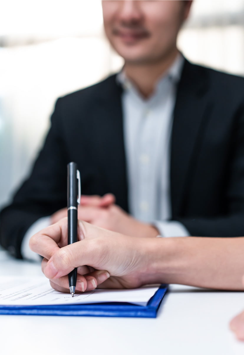 Close-up of signing a document with a pen while another person observes, symbolizing agreement.