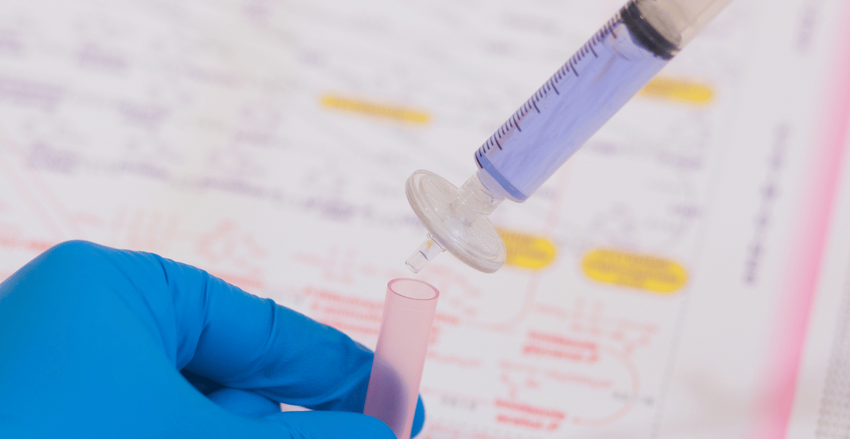 Gloved hand holding a tube while using a syringe with a syringe filter.