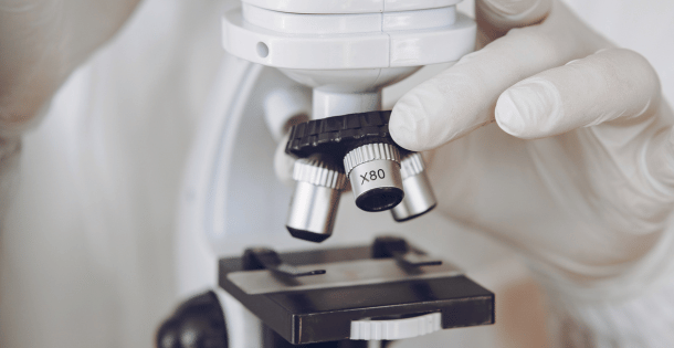 A gloved hand adjusting a microscope in a lab, emphasizing the use of syringe filters