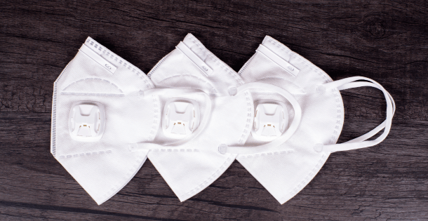 Four white respirators arranged in a row on a wooden surface.