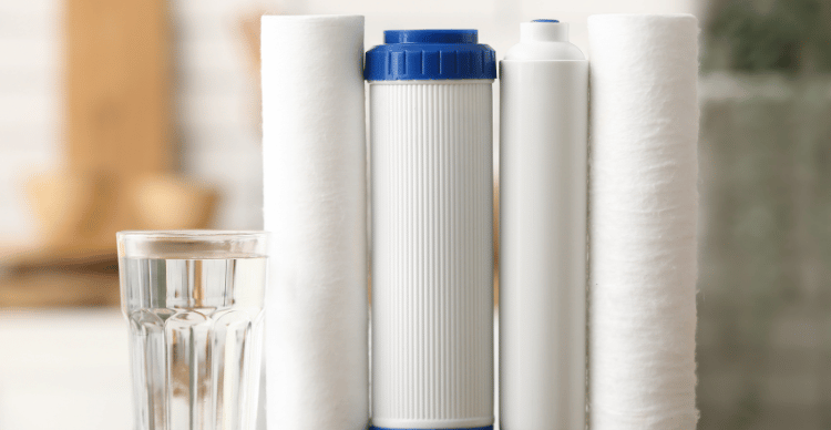 A set of water filters, including a syringe filter, next to a glass of clear water.