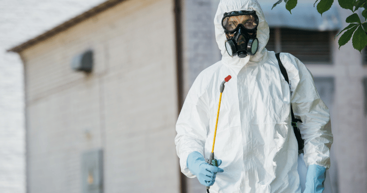 A person in protective gear wearing a respirator and holding a sprayer