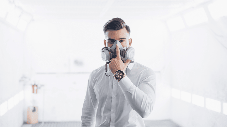 Man in a white shirt adjusting a respirator mask in a bright, airy room.